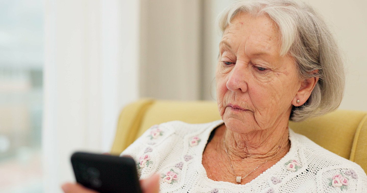 Foto einer älteren Frau, die auf ihr Handy schaut.
