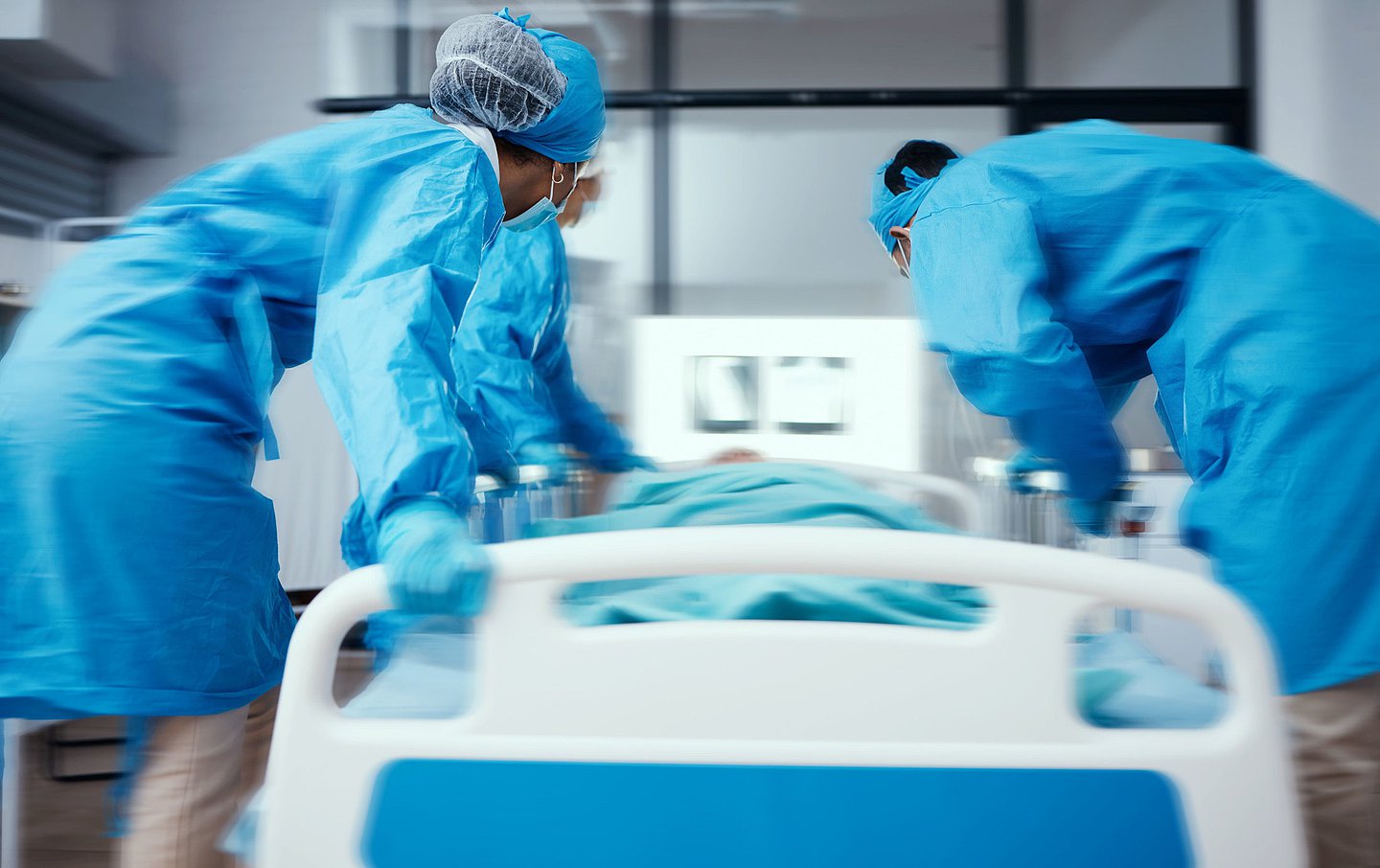 Das Foto zeigt Krankenpflegerinnen und Krankenpfleger, die einen Patienten im Krankenbett in Eile ins OP schieben.