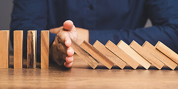 Eine Hand stoppt umfallende Holz-Dominosteine.