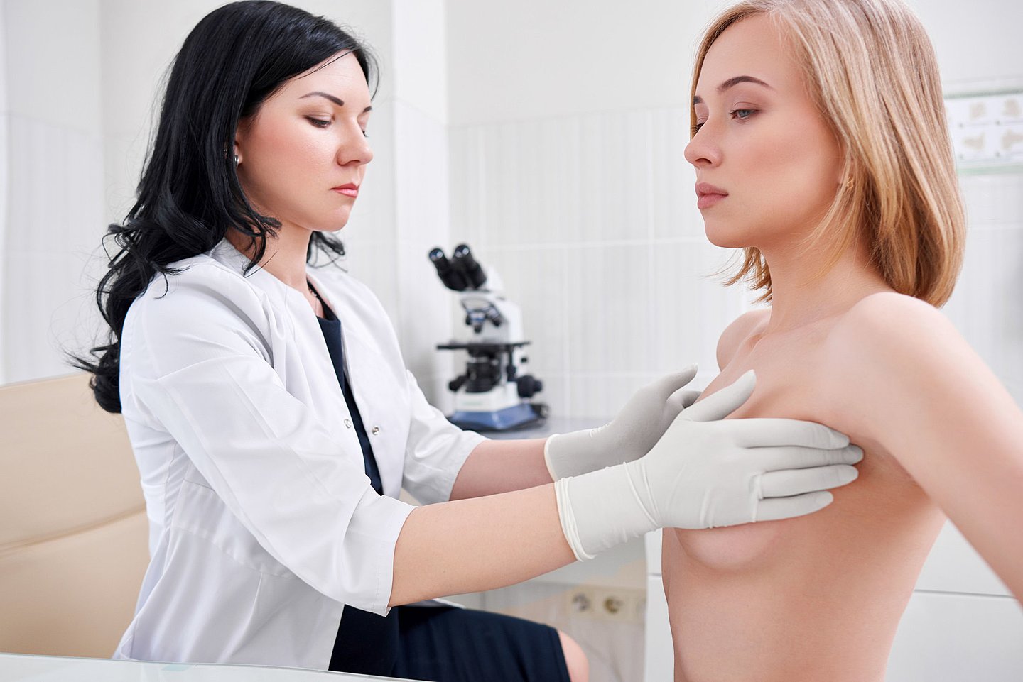 Eine Ärztin untersucht und tastet die Brust einer Patientin ab, die vor ihr steht.
