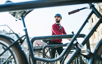 Ein Mann steht mit einem Fahrrad an einem Fahrradb&uuml;gel.