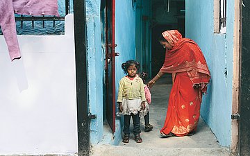 Eine enge Häusergasse: Eine Frau im Sari steht neben ihren zwei kleinen Töchtern.
