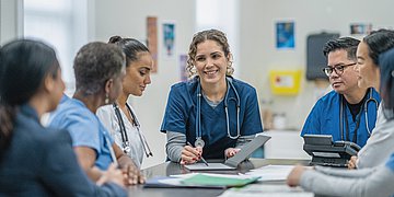 Primärversorgung erfolgt im großen Team Ein Team von Medizinkräften steht an einem Tisch und bespricht sich.
