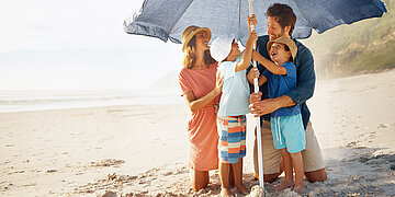 Eine Familie am Strand stellt einen Sonnenschirm auf.