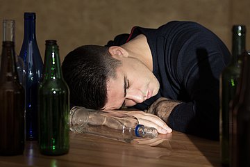 Rauschtrinken Ein Jugendlicher liegt schlafend auf einem Tisch mit leergetrunkenen Flaschen.