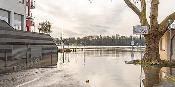 Foto: Blick auf einen &uuml;ber die Ufer getretenen Flu&szlig;, daneben ein Geb&auml;ude.