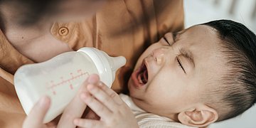 Kuhmilchallergie Ein Säugling wird mit der Flasche gefüttert und schreit.