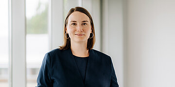 Frau Schenk schaut frontal in die Kamera, hinter ihr ist ein Fenster.