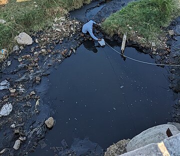 Luftaufnahme eines Mannes, der einem stark verschmutzten Gewässer in Indien eine Wasserprobe entnimmt.