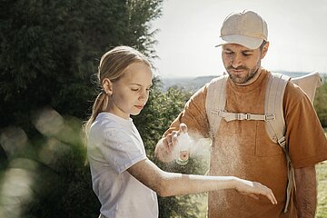 Ein Mann pr&auml;pariert den Arm eines M&auml;dchens mit Zeckenspray.