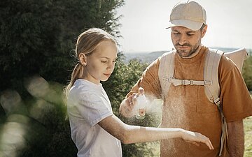 Ein Mann pr&auml;pariert den Arm eines M&auml;dchens mit Zeckenspray.