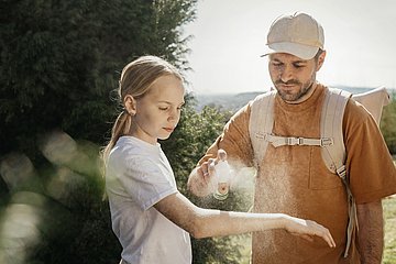 Zeckenspray Ein Mann präpariert den Arm eines Mädchens mit Zeckenspray.