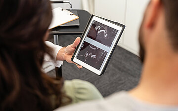 Zwei Personen schauen auf einem Tablet Bilder einer medizinischer Untersuchung an.