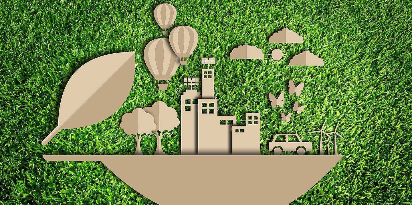 Illustration: Verschiedene Scherenschnitte von Symbolen, die Bestandteile einer Kommune darstellen, wie Häuser, ein Auto, Windräder und Bäume, in brauner Farbe stehen auf einer Art Schiff vor dem Hintergrund einer grünen Wiese.