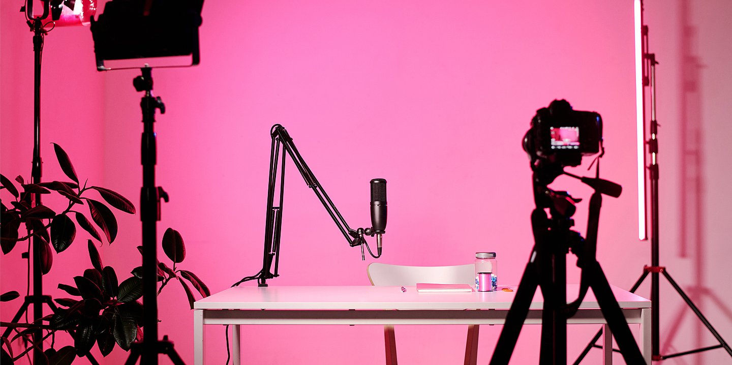 Foto: Studio mit Lichtausleuchtung, aufgebauter Kamera und Mikrofon an einem Tisch – alles pink ausgeleuchtet.