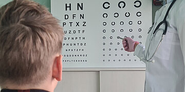Ein Junge macht ein Sehtest, ihm gegen&uuml;ber steht eine &Auml;rztin.