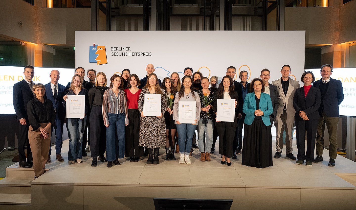 Großes Gruppenfoto: Alle Preisträgerinnen und Preisträger, Laudatorinnen und Laudatoren und Initiatoren auf der Bühne im Atrium des AOK-Bundesverbandes in Berlin