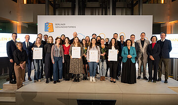 Gro&szlig;es Gruppenfoto: Alle Preistr&auml;gerinnen und Preistr&auml;ger, Laudatorinnen und Laudatoren und Initiatoren auf der B&uuml;hne im Atrium des AOK-Bundesverbandes in Berlin