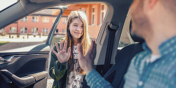 Foto: Ein M&auml;dchen verabschiedet sich an der offenen Autot&uuml;re von ihrem Vater.