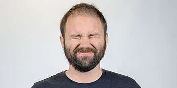 Foto: Portr&auml;taufnahme von einem Mann, der sein Gesicht zusammenkneift.