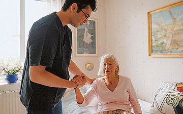 Pflegequalität Foto einer jungen Mannes, der einer alten Dame vom Bett aufhilft