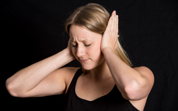 Ohren vor Lärm schützten Foto: Eine Frau hält sich beide Ohren zu.