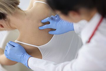Das Foto zeigt eine &Auml;rztin in Nahaufnahme, die bei einer jungen Patientin die obere Wirbels&auml;ule untersucht.