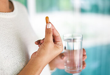 Eine Frau in Nahaufnahme h&auml;lt ein Glas Wasser und eine Tablette in der Hand.