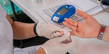 EIne Person mit wei&szlig;en Handschuhen testet den Blutzuckergehalt einer Diabetes Person.