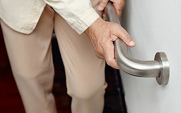 Pflege in Familien fördern Foto einer alten Frau, die sich an einem Treppengeländer festhält