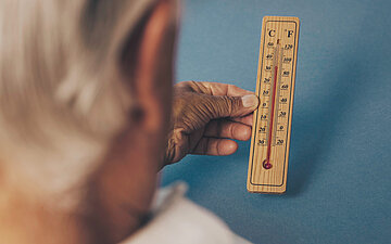 Foto: Eine &auml;ltere Person h&auml;lt ein Thermometer in der Hand, das circa 35 Grad anzeigt.