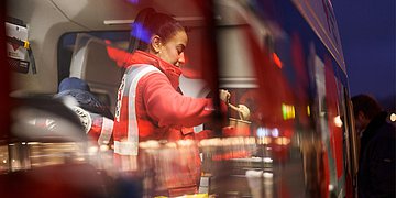 Eine Mitarbeiterin der Bahnhofsmission steht in einem Wärmebus und füllt heißen Brei in einen Becher. Sie trägt eine Arbeitsjacke.