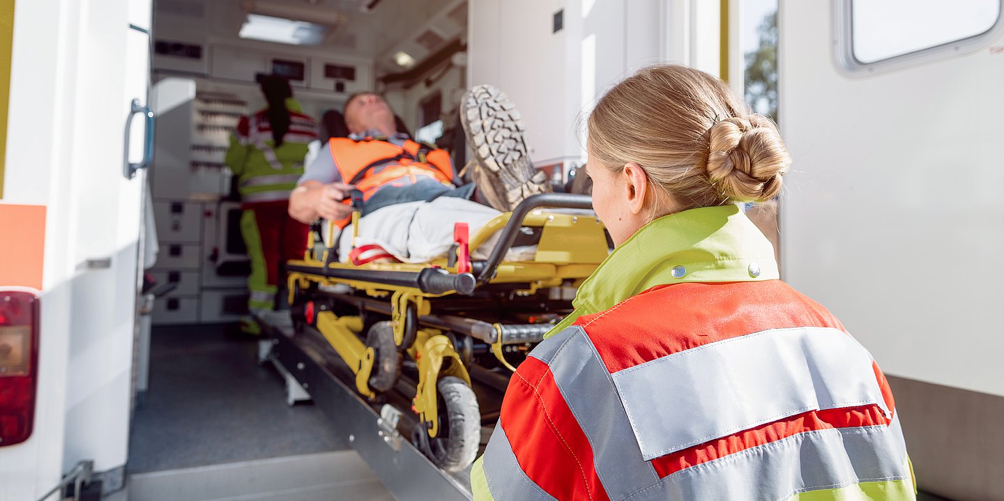 Eine Rettungskraft schiebt eine Trage, auf der ein Mann liegt, in ein Einsatzfahrzeug.