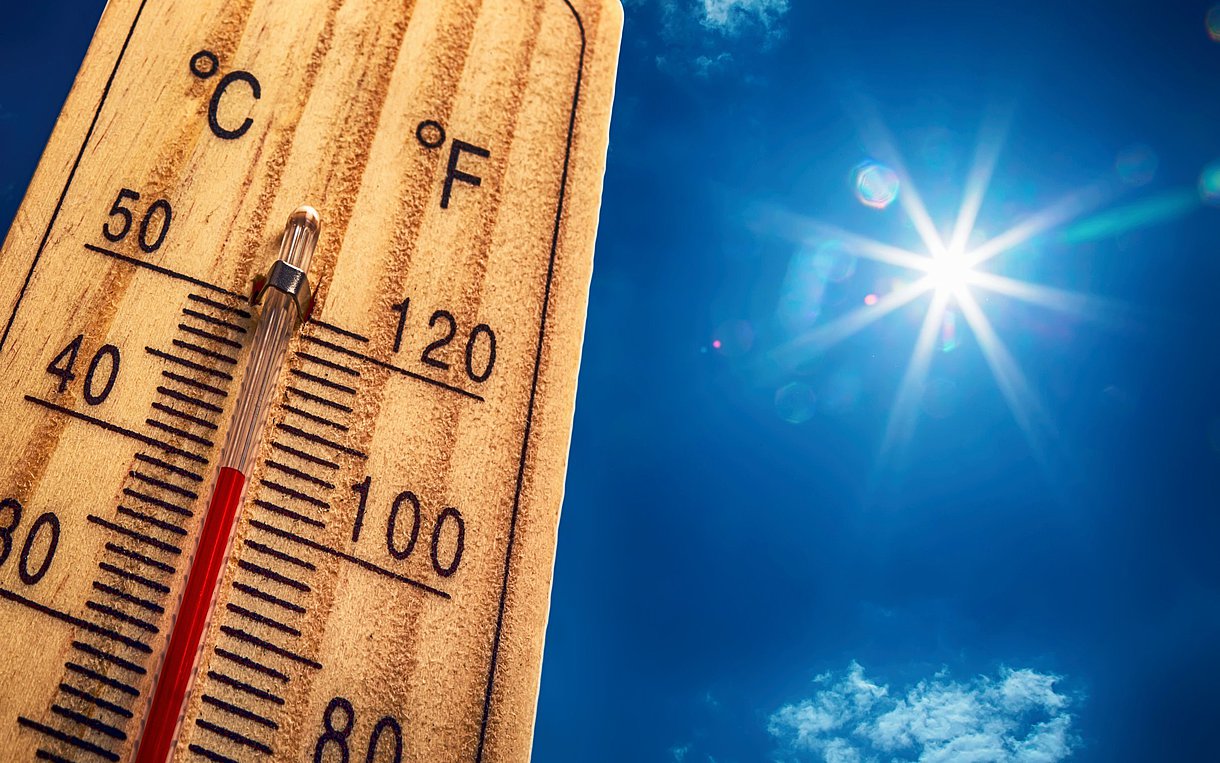 Auf dem Foto ist ein Thermometer mit blauem Himmel und Sonne im Hintergrund zu sehen.