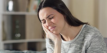 Trigeminusneuralgie Eine Frau fasst sich ein eine Gesichtshälfte und macht ein schmerzverzerrtes Gesicht.