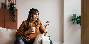 Eine Frau nutzt bei einer Tasse Kaffee ihr Smartphone.