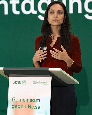 Yeliz Kidis steht hinter einem Rednerpult auf der B&uuml;hne der Fachtagung.