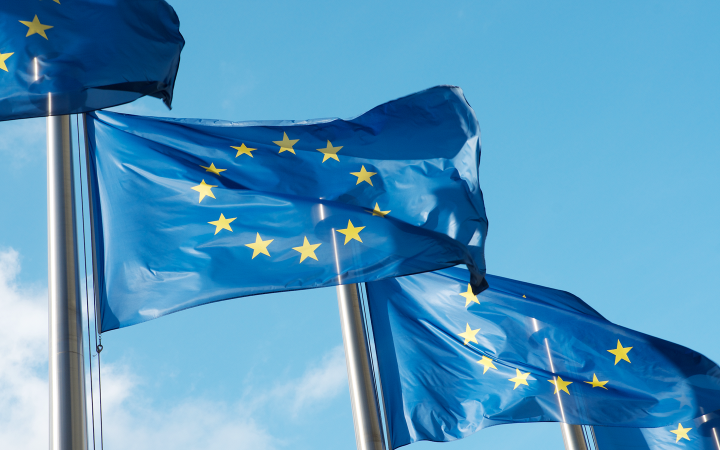 Drei Europa-Fahnen am Mast wehen im Wind vor blauem Himmel, eine davon im Anschnitt