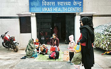 Auf einem Teppich vor einem Gebäude des Vikas Health Centre sitzen mehrere Mütter mit ihren Kindern.