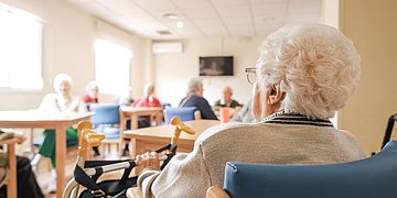 Foto: Blick in einen Aufenthaltsraum, in dem mehrere Seniorinnen und Senioren sitzen.