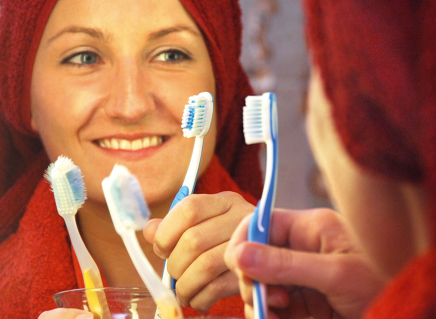 Eine Frau hält lächelnd eine Zahnbürste in der Hand. Mehrere Zahnbürsten sind noch im Bild.