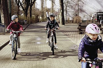 Drei Kinder fahren mit dem Fahrrad &uuml;ber einen gepflasterten Weg.