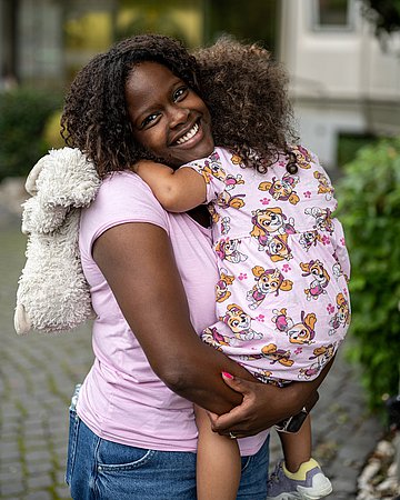 Cochlea-Implantat Foto einer jungen Frau, die ihre kleine Tochter im Arm hält und lächelt