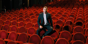 Foto: Professor Dr. David Matusiewicz sitzt auf der Sessellehne im Colosseum Theater Essen.