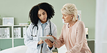 Eine &Auml;rztin zeigt einer Patientin Resultate auf einem Tablet