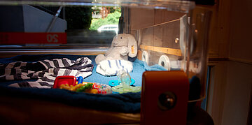 Ein W&auml;rmebett im Innenraum der KiTa. In ihm liegen ein Kuscheltier, ein Schlafsack, Spielzeug und Schnuller.