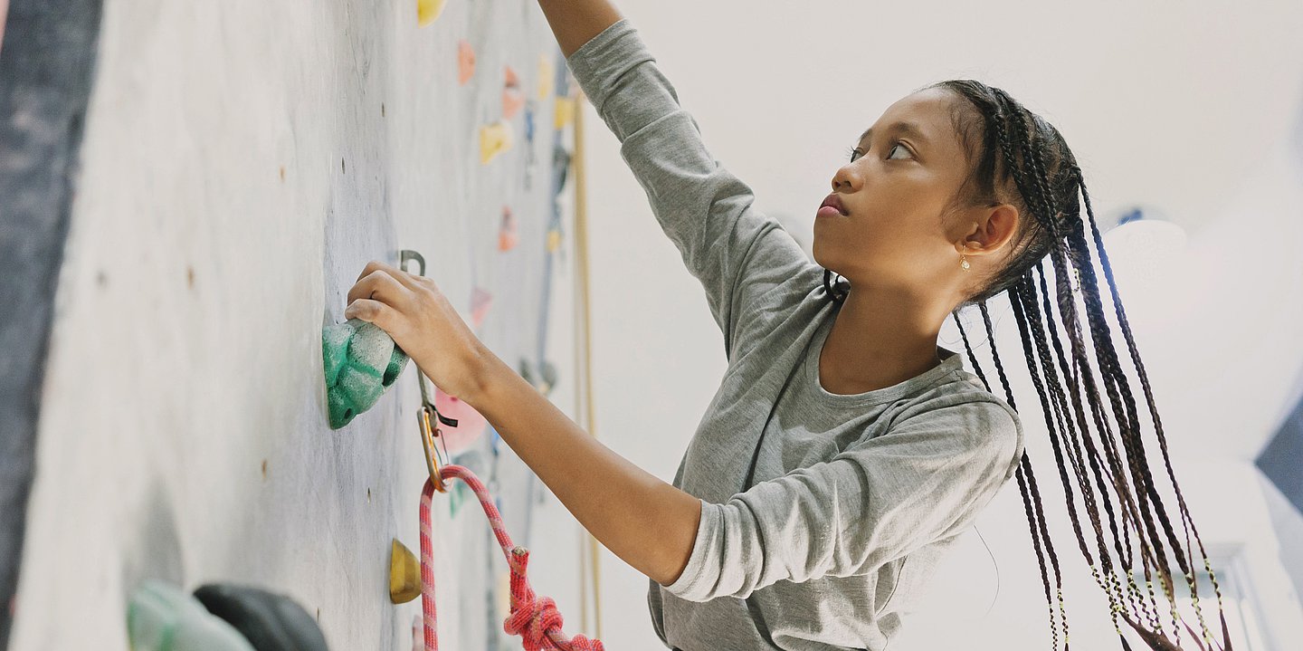 Ein Mädchen klettert eine künstliche Kletterwand hinauf.