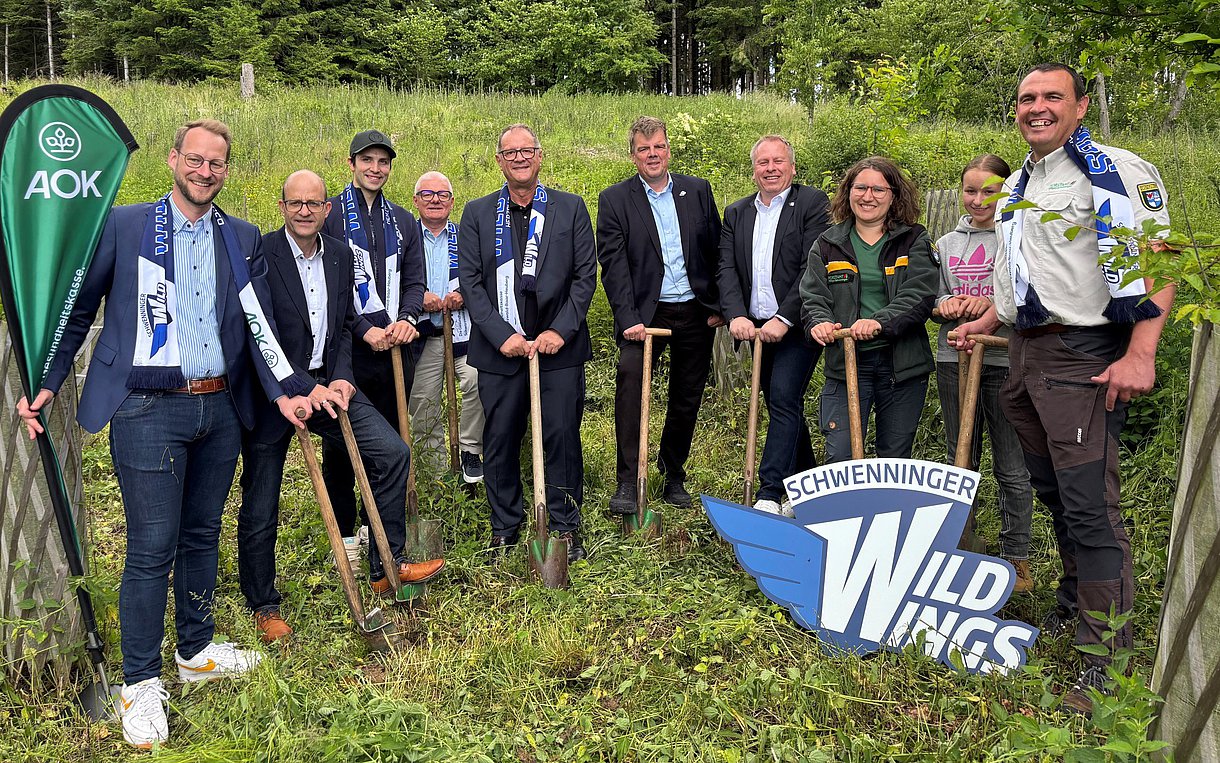 Eine Gruppe von Menschen steht vor einem Wald um Bäume zu pflanzen.