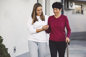Foto zeigt eine Pflegebed&uuml;rftige beim Spaziergang in Begleitung mit ihrer Angeh&ouml;rigen