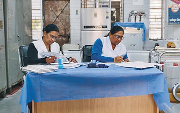 In einem Praxiszimmer sitzen zwei Frauen an einem Tisch und arbeiten in Berichten.